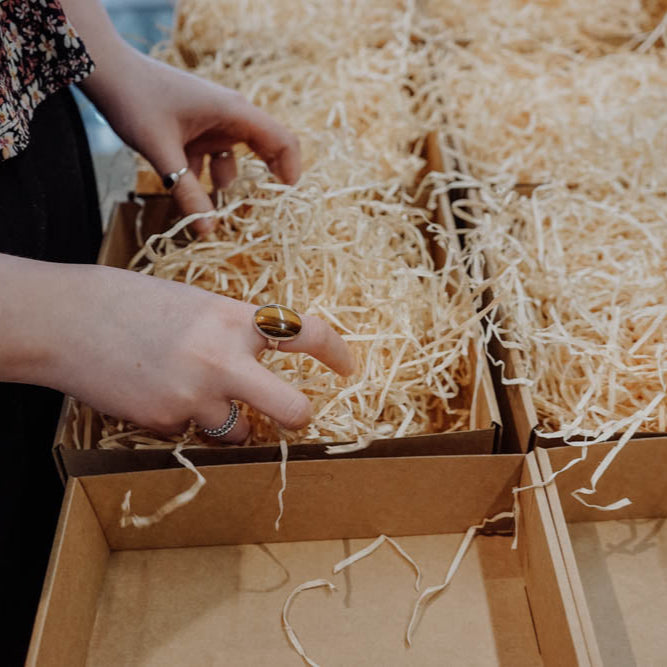 Person packing items into a cardboard box filled with shredded paper