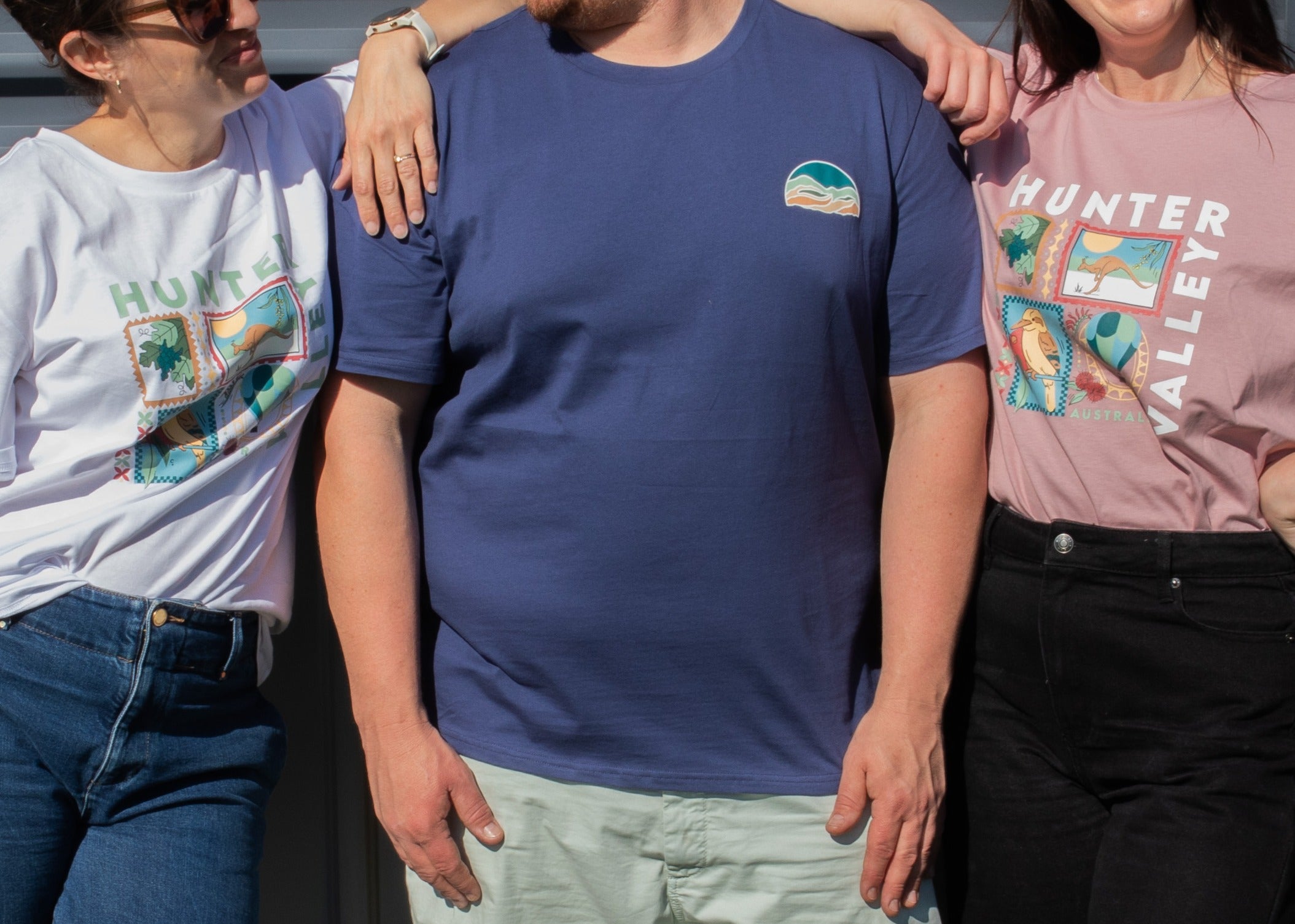 Three models wearing Hunter Valley t-shirts in a side-by-side comparison. The center model wears a navy blue crewneck t-shirt with a small multicolor landscape logo on the left chest.